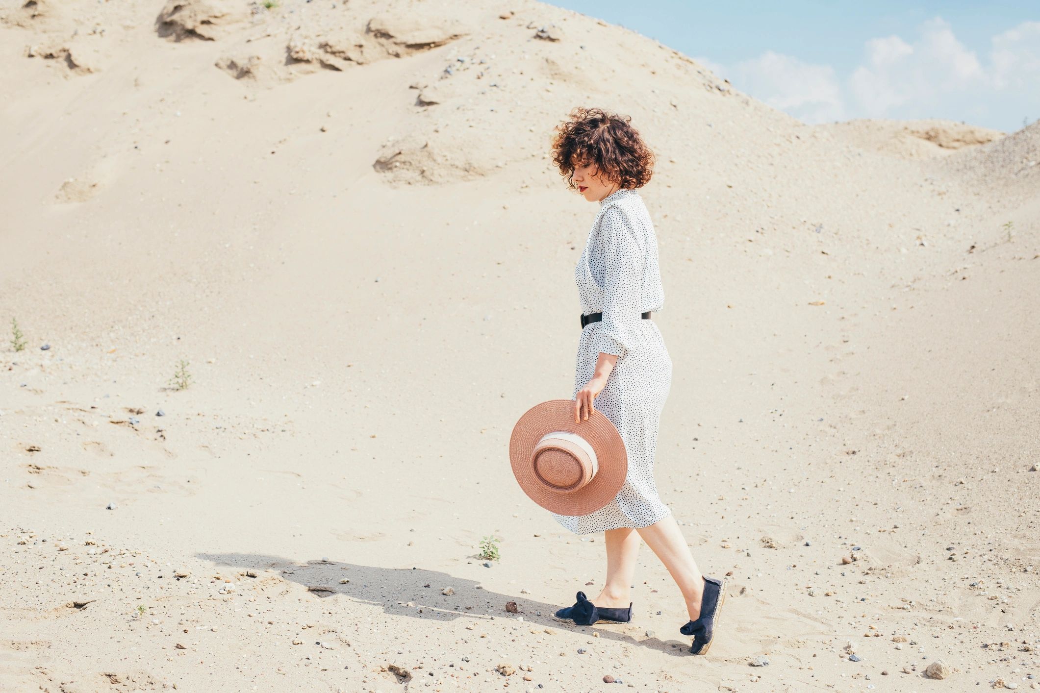 Woman in a polka dot dress walking in a desert with a sun hat