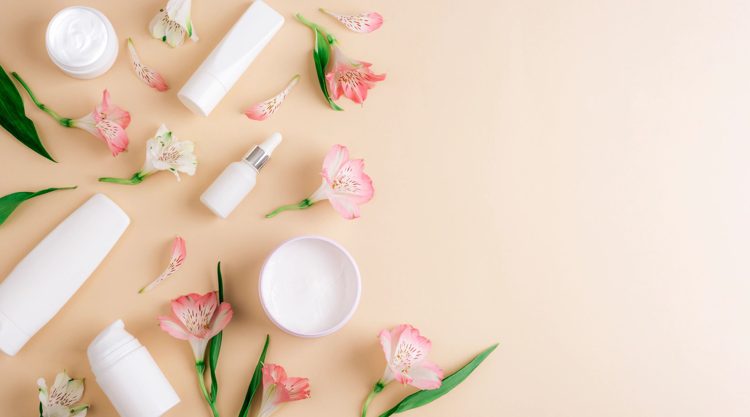 Skincare products with flowers in a minimal flat lay